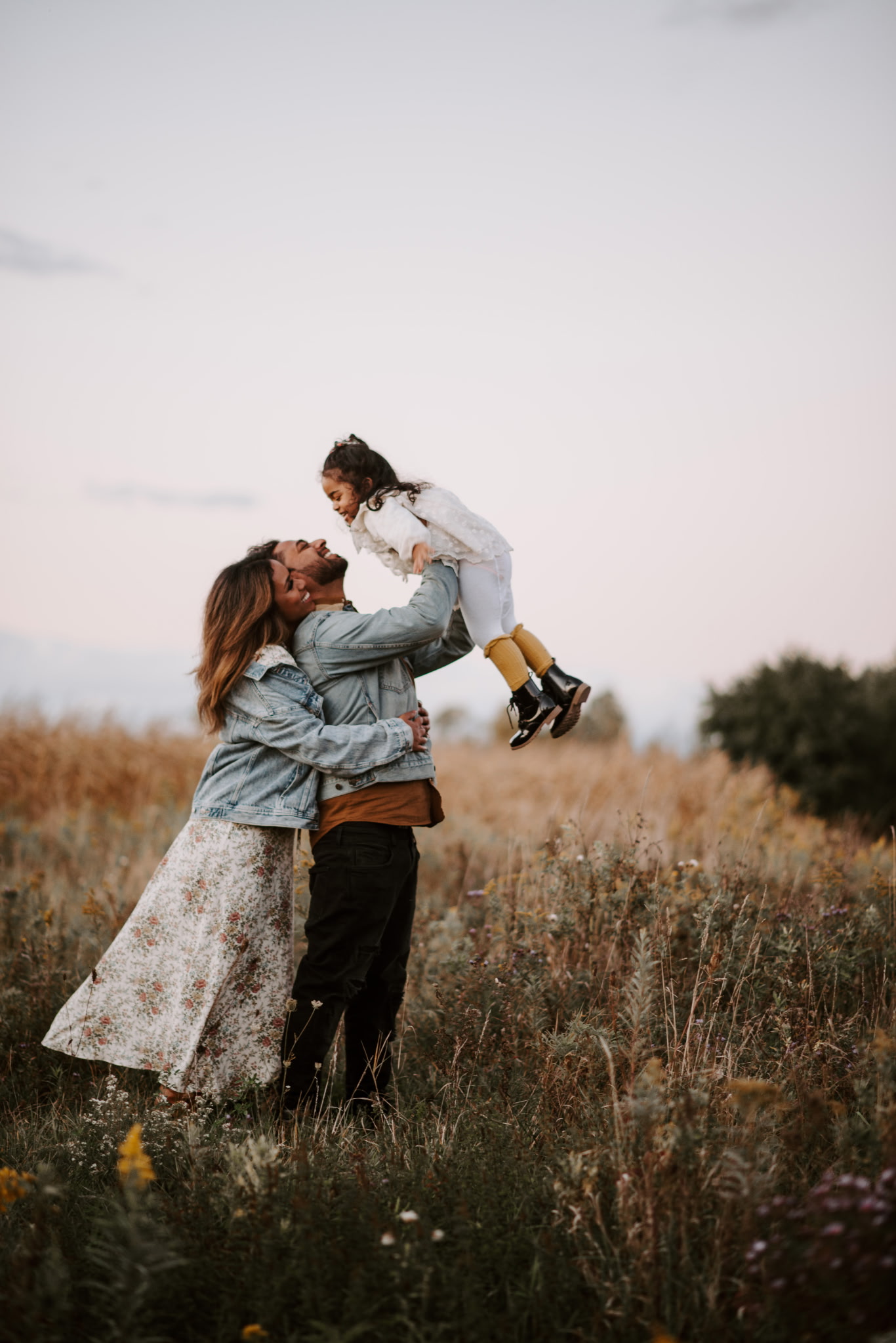 Parents sharing a playful moment with their young daughter in a meadow