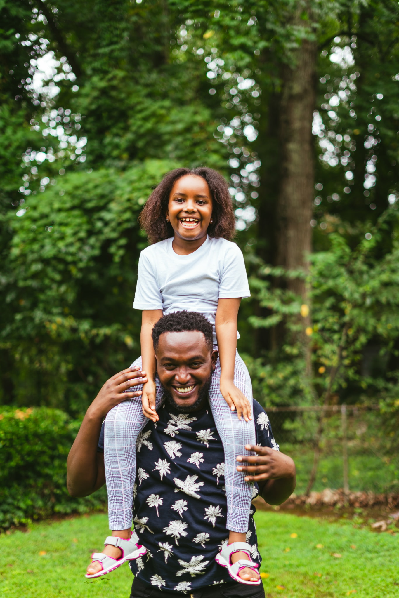 A smiling father carrying his daughter on his shoulders outdoors